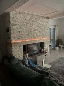 Création 100 % sur mesure de cette cheminée avec parement pierre, chêne et éclairage LED.